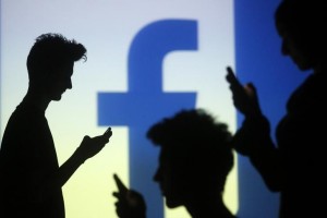 People pose with mobile devices in front of projection of Facebook logo in this picture illustration taken in Zenica